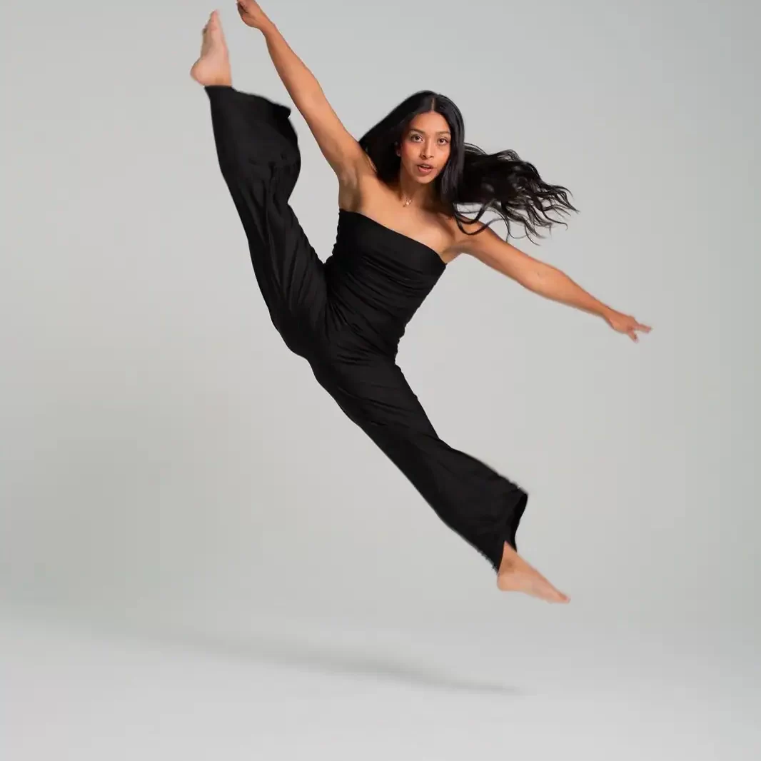 La bailarina Valeria Vázquez en medio de un gran salto o "Split Leap" en un estudio, vestida de negro, con las piernas abiertas en el aire.
